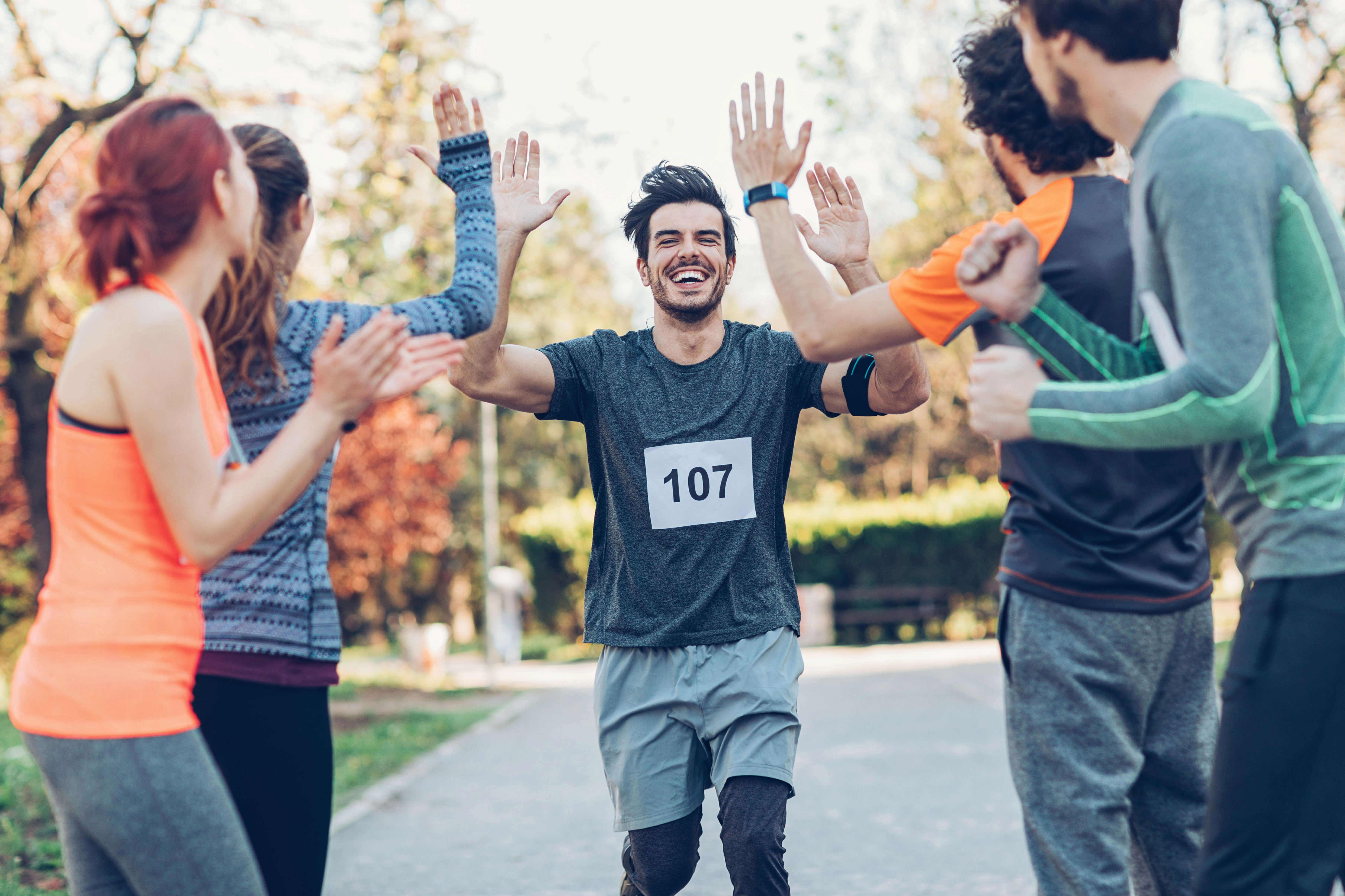 Junger Mann joggt ins Ziel, seine Freunde klatschen ihn ab