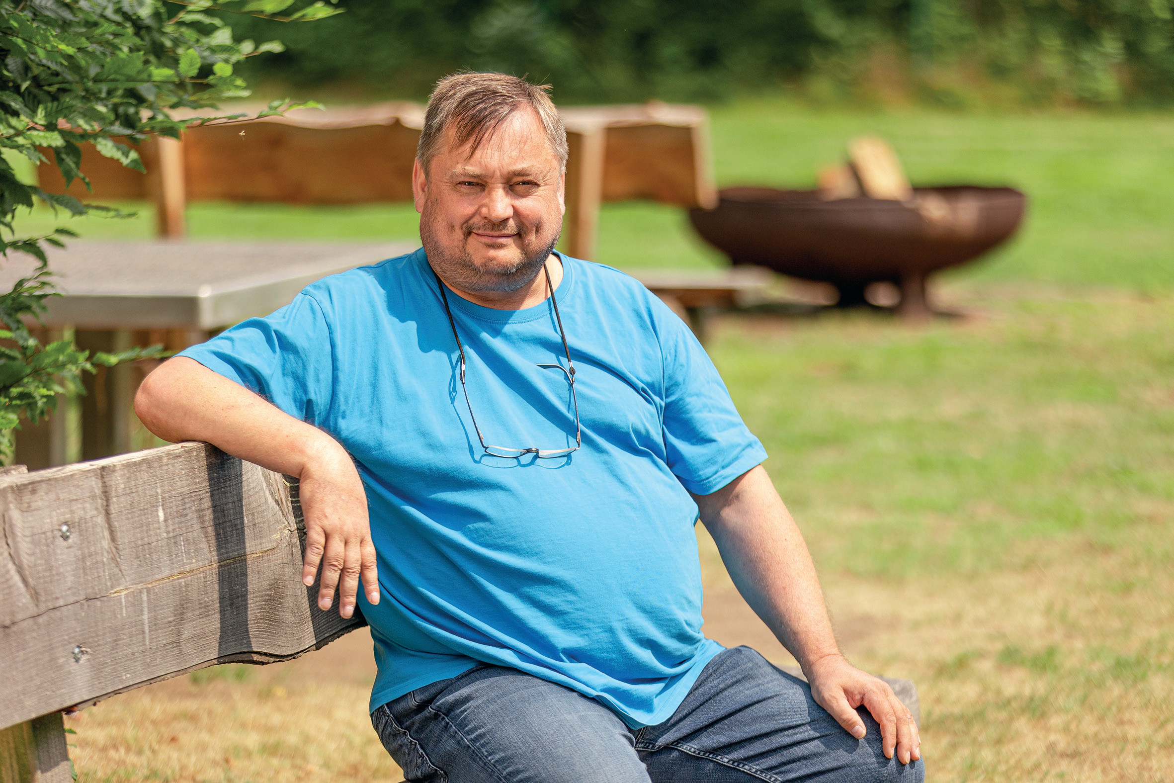 Mann sitzt bei sonnigem Wetter auf einer Bank in der Natur