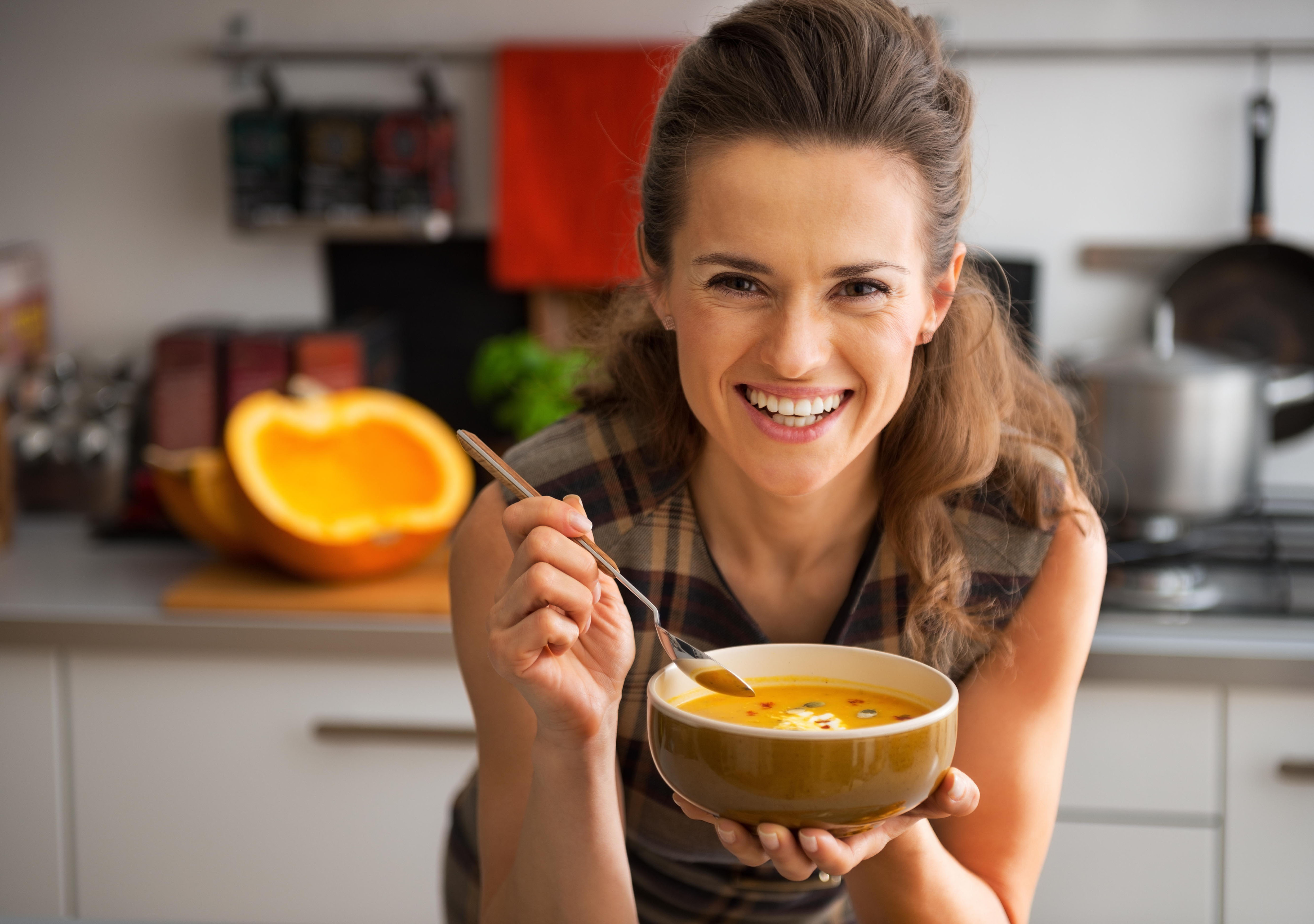 Lachende junge Frau mit einer Schüssel Kürbissuppe in der Hand